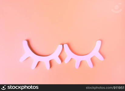 White wooden closed eyes with eyelashes in neon pink light on pastel background. Stylish wall decor. Top view, flat lay. Concept of vivid sweet dreams. Accessories for kids room. Minimal style.