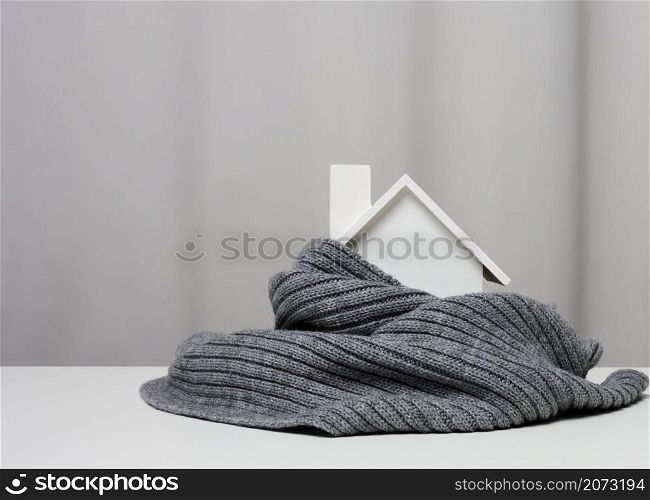 white wooden miniature house wrapped in a gray knitted scarf. Building insulation concept, loans for repairs