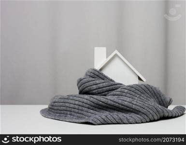 white wooden miniature house wrapped in a gray knitted scarf. Building insulation concept, loans for repairs