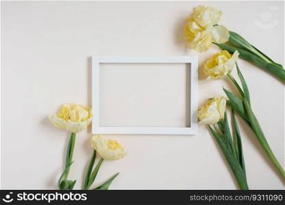 White wooden photo frame framed with yellow tulip flowers on a light table. Flat lay, card