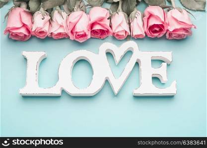 White word LOVE with pastel pink roses on turquoise blue background, top view. Modern minimal flat lay concept