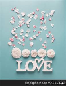 White word sign LOVE with pale roses and petals on turquoise blue background, top view. Modern minimal flat lay concept