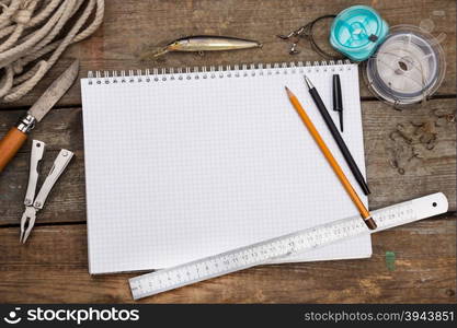 white writing-book with fishing tackles and design tools on wooden board. for mockup, print, design.