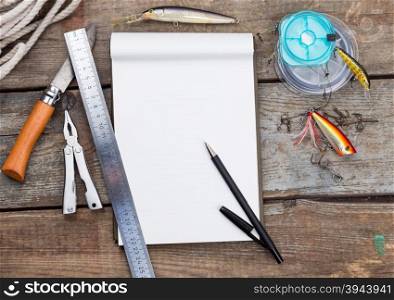 white writing-book with fishing tackles and design tools on wooden board. for mockup, print, design.