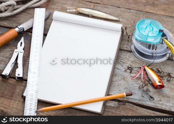 white writing-book with fishing tackles and design tools on wooden board. for mockup, print, design.