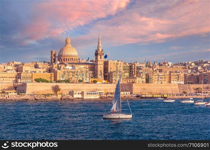 White yacht and Old town of Valletta with churches of Our Lady of Mount Carmel and St. Paul&rsquo;s Anglican Pro-Cathedral at sunset, Valletta, Capital city of Malta. Valletta Skyline from Sliema at sunset, Malta