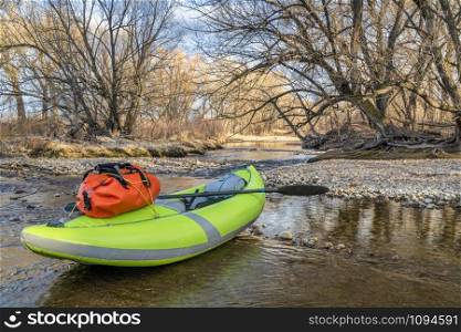 whitewater inflatable kayak with a paddle and waterproof duffel on a river shore - Poudre River in Fort Collins, Colorado in early spring scenery and low water, water sports and recreation concept