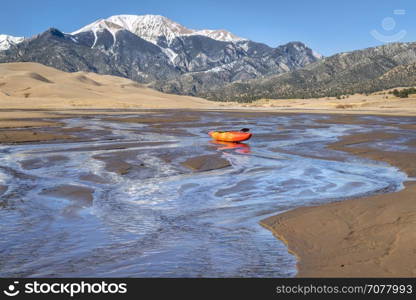 whitewater kayak in shallow waters of Medano Creek with Great Sand Dunes and Sangre de Cristo Mountains in background