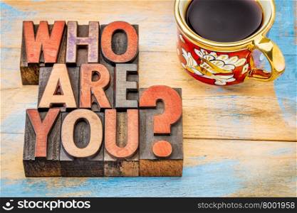 who are you question - word abstract in letterpress wood type blocks against grunge painted wood with a cup of coffee
