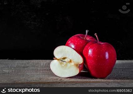 Whole and cut in half apple lying on textured wooden table on dark background