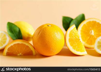 Whole and cut oranges and lemons with green leaves on orange color background, fresh and healthy in summer light concept.