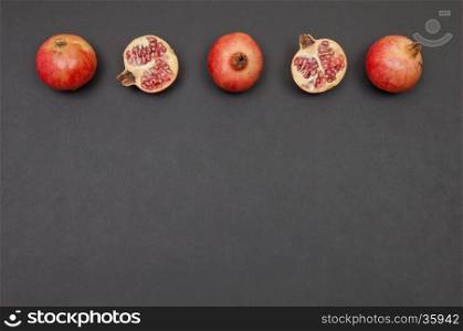 Whole and cut pomegranates in a row on dark grey background
