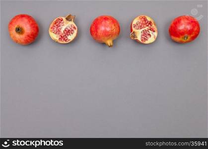 Whole and cut pomegranates in a row on grey background