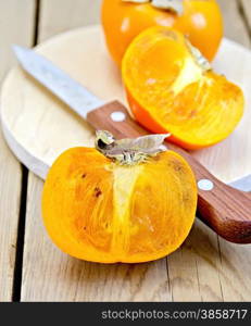 Whole and half a persimmon fruit, knife on a round board on a wooden boards background