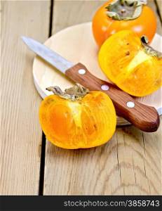 Whole and half a persimmon fruit, knife on a wooden boards background