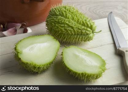 Whole and half spined fresh chayote fruit on a cutting board