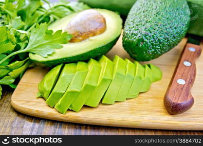 Whole and halved avocado with bone, sliced avocado half, knife, parsley, napkin on a wooden boards background