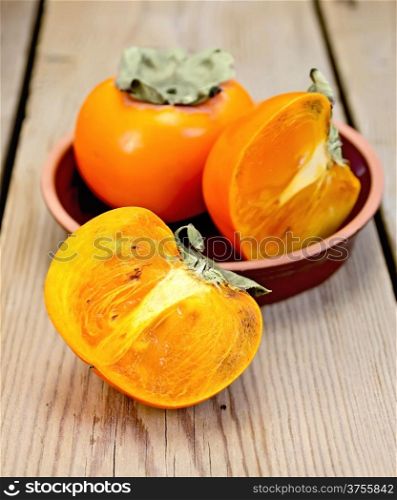 Whole and halves of persimmon in pottery on the background of wooden boards