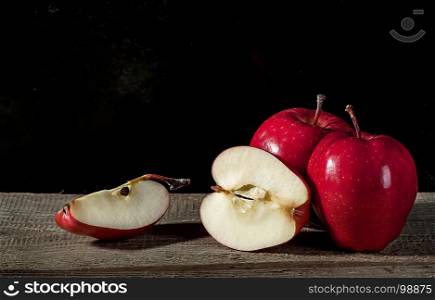 Whole and several pieces of apple lying on textured wooden table on dark background