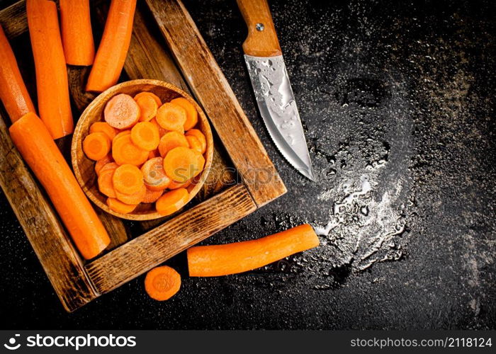 Whole and sliced carrots on a wooden tray. On a black background. High quality photo. Whole and sliced carrots on a wooden tray.