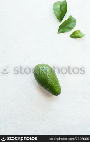 Whole avocado with leaves on white table background, top view. Healthy food ingredient