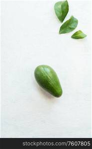 Whole avocado with leaves on white table background, top view. Healthy food ingredient