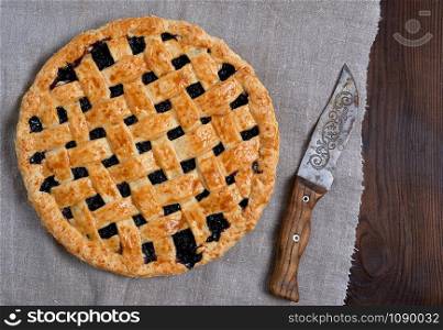 whole baked round black currant cake on brown wooden background, top view