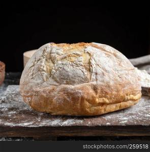 whole baked round bread made from white wheat flour on a wooden board, black background