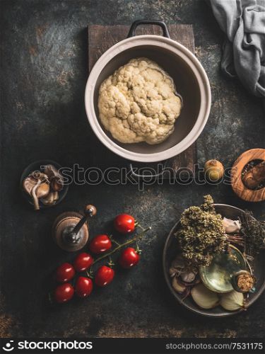 Whole cauliflower in cooking pot on dark rustic kitchen table background with vegetarian ingredients.Top view