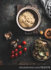 Whole cauliflower in cooking pot on dark rustic kitchen table background with vegetarian ingredients.Top view