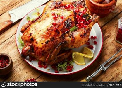 Whole chicken baked with pomegranate berries in plate on a wooden rustic old background.. Roasted chicken on plate