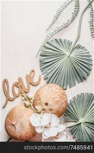 Whole coconuts with tropical leaves, white orchid flowers and word love on white desk, top view. Copy space for your design or product. Healthy lifestyle layout