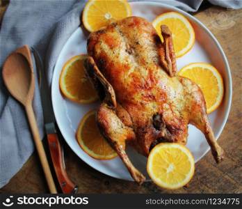 Whole crispy golden roast duck with marinated with fresh orange slices for a festive . Top view rustic wooden background.