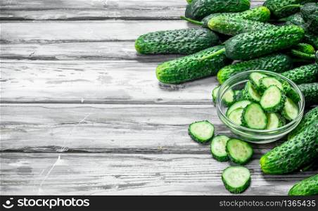 Whole cucumbers and cucumber slices in the bowl. On wooden background. Whole cucumbers and cucumber slices in the bowl.