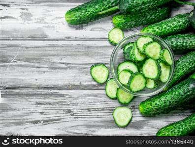 Whole cucumbers and cucumber slices in the bowl. On wooden background. Whole cucumbers and cucumber slices in the bowl.