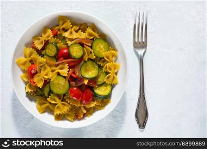 Whole farfalle pasta with zucchini, cherry tomatoes and red onion seen from above. Whole farfalle pasta with zucchini, cherry tomatoes and red onion