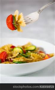Whole farfalle pasta with zucchini, cherry tomatoes and red onion suspended on the fork. Whole farfalle pasta with zucchini, cherry tomatoes and red onion