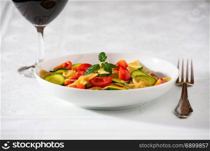Whole farfalle pasta with zucchini, cherry tomatoes and red onion with a red wine glass. Whole farfalle pasta with zucchini, cherry tomatoes and red onion