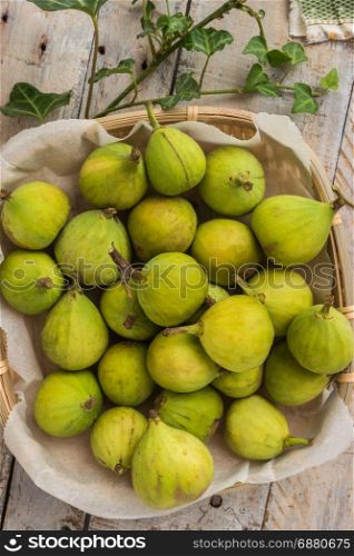 Whole figs in wicker basket on top of a rustic wooden table.
