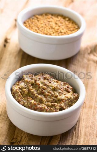 Whole grain mustard and yellow mustard seeds in small bowls, photographed on wood with natural light (Selective Focus, Focus in the middle of the mustard)