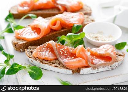 Whole grain rye bread open sandwiches with salted salmon on a white rustic wooden table. Healthy food