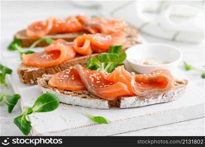 Whole grain rye bread open sandwiches with salted salmon on a white rustic wooden table. Healthy food