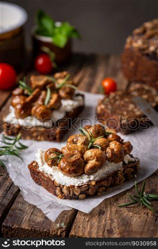 Whole grain rye bread toast with cream cheese or ricotta, mushroom and herbs on rustic wooden background.. toast with cream cheese and mushroom