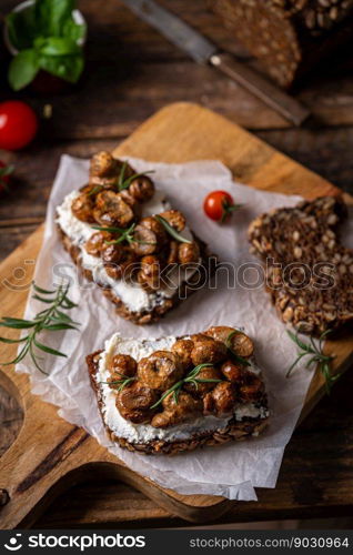 Whole grain rye bread toast with cream cheese or ricotta, mushroom and herbs on rustic wooden background.. toast with cream cheese and mushroom