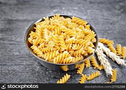Whole grain wheat flour fusilli pasta in a bowl, spikelets of wheat on wooden board background