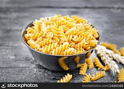 Whole grain wheat flour fusilli pasta in a bowl, spikelets of wheat on a dark wooden board background