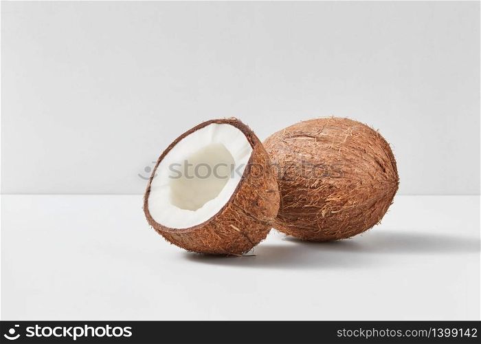 Whole natural exotic ripe coconut fruit with half on a duotone light grey background with soft shadows, copy space. Vegetarian concept.. Fresh ripe organic coconut fruits on a gray duotone background.