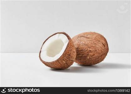 Whole natural exotic ripe coconut fruit with half on a duotone light grey background with soft shadows, copy space. Vegetarian concept.. Fresh ripe organic coconut fruits on a gray duotone background.