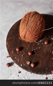 Whole organic coconut and chocolate balls on a wooden board is not snrrom kitchen table with copy space. Exotic walnut coconut and chocolate balls on an old wooden board on a gray concrete background
