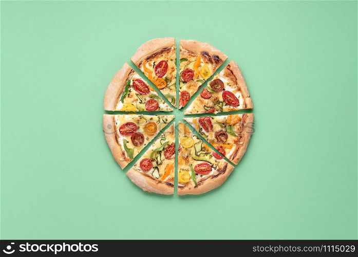 Whole pizza primavera cut in slices on a green background. Above view of vegetarian pizza. Italian cuisine. Pizza with cherry tomatoes. Homemade food.